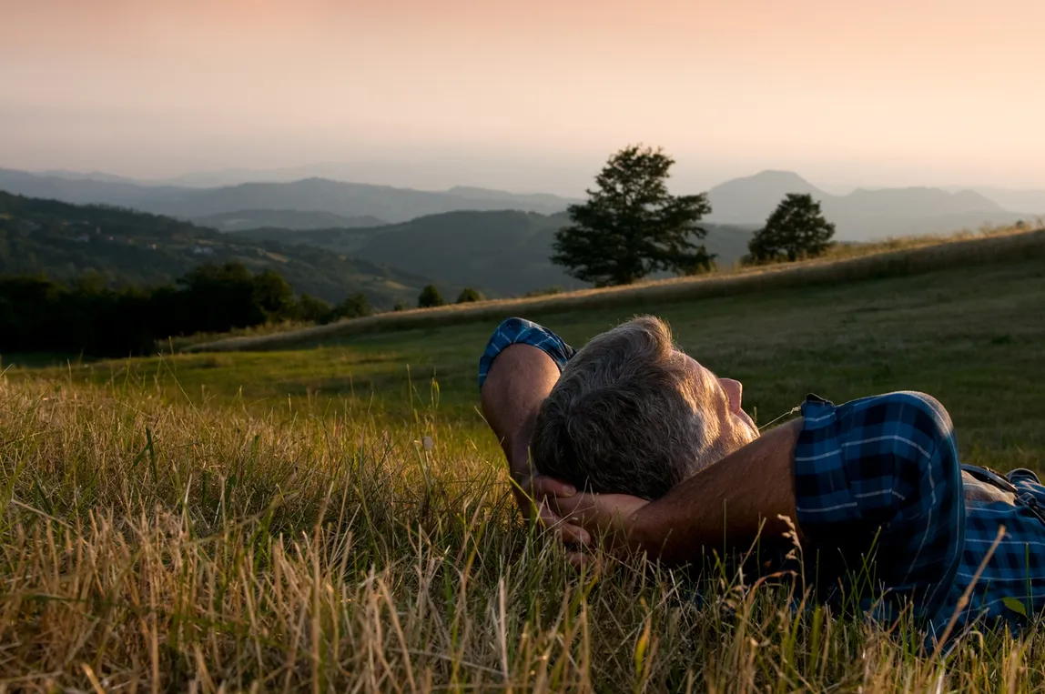 Older man relaxing comfortably on a grassy hillside at sunset